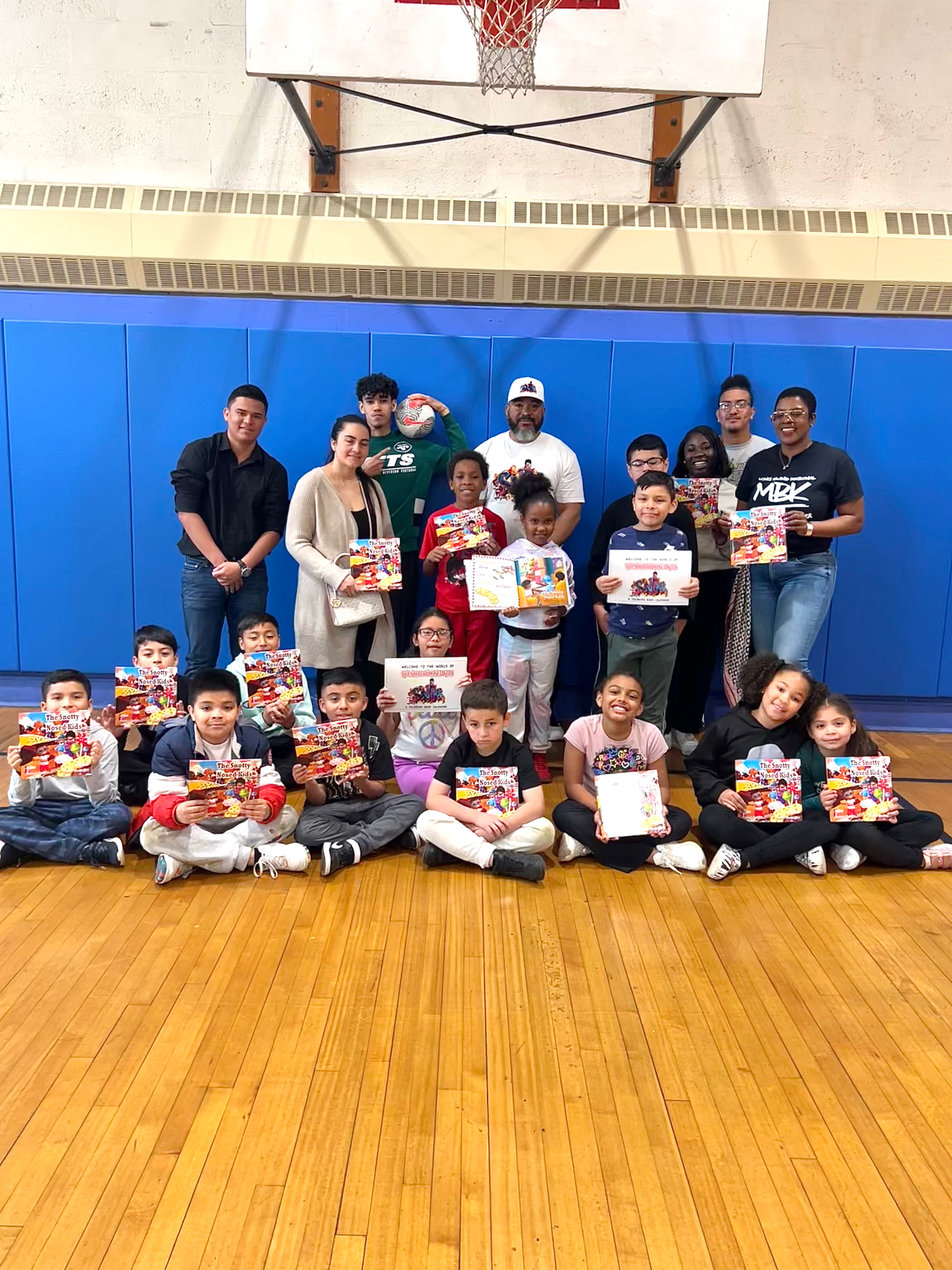 Group of people and children holding books in a gymnasium.